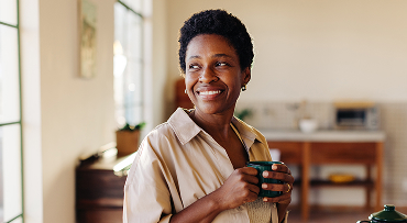A person standing in a kitchen smiling while holding a cup of coffee.