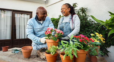 Man and woman standing at a table potting flowers and laughing.